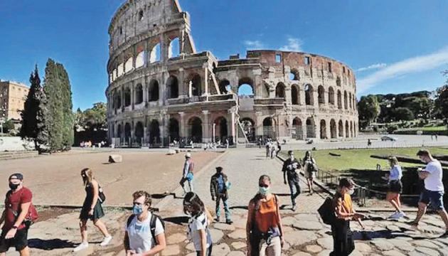 People wearing face masks walk past the Colosseum in Italy.