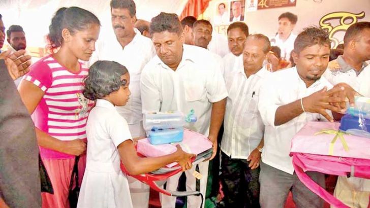Minister Sajith Premadasa distributes school bags and other items to students, at the opening of a model village.
