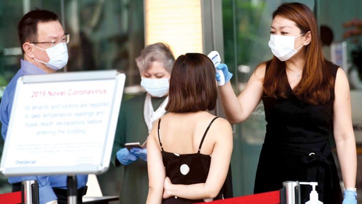 Building management staff conduct temperature screenings of visitors and tenants of a building in the financial district of Singapore on Saturday in the wake of the spread of the COVID-19.
